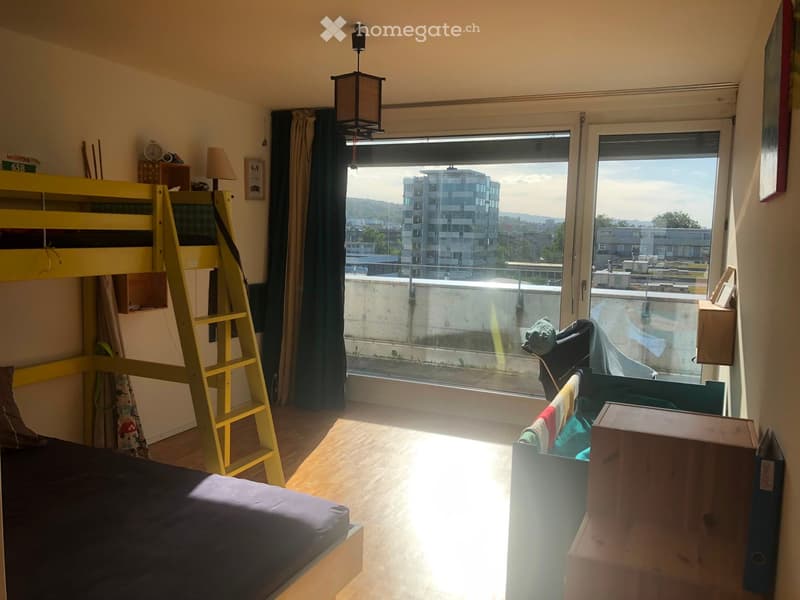 Bright bedroom with a bunk bed, a small table, and a large window offering a city view.