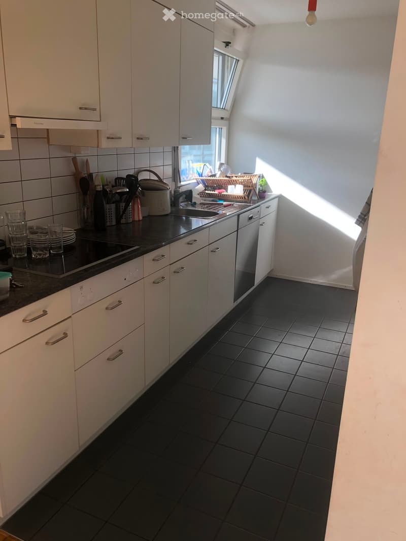 Modern kitchen with white cabinets, black tiled floor, and black countertops. Features a sink, dishwasher, and various kitchen utensils on the counter.