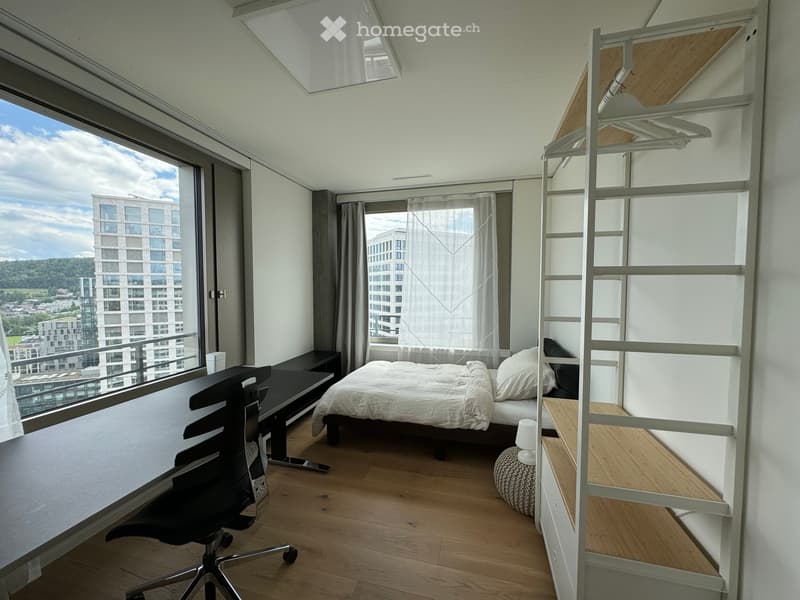 Modern bedroom with a bed, desk, chair, and shelving unit. Large windows offer a view of the city and surrounding landscape.