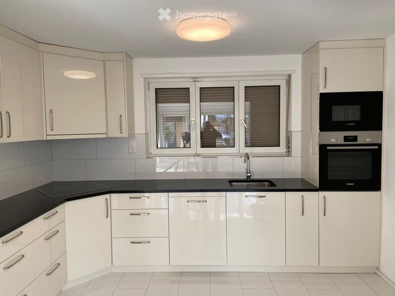 Modern kitchen with white cabinets, black countertops, stainless steel appliances, and a large window with blinds.