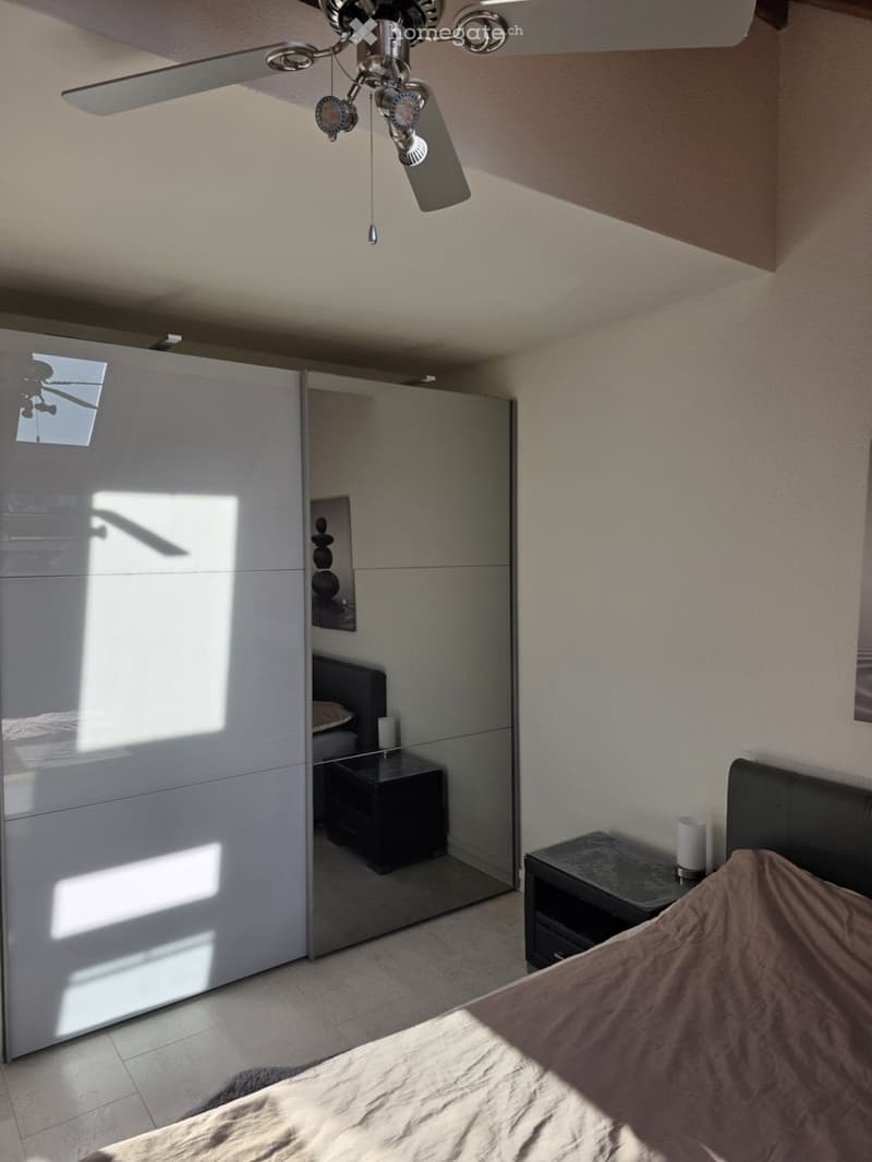 Modern bedroom with a large bed, nightstands, a sleek wardrobe, and a ceiling fan with lights.