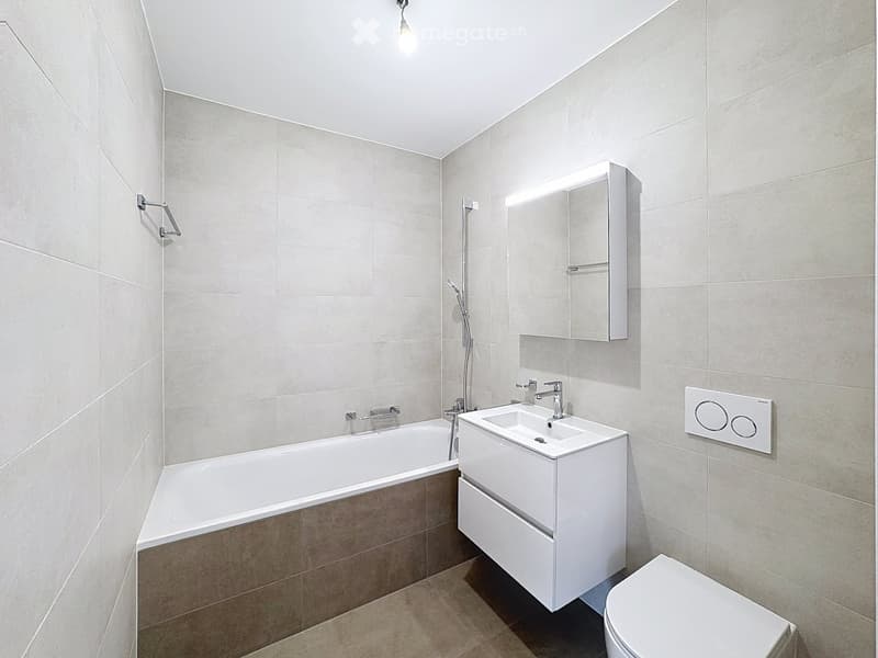 Modern bathroom with a bathtub, sink, toilet, and a built-in mirror cabinet. Light-colored tiles and sleek fixtures.