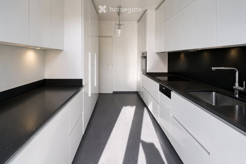 Modern kitchen with white cabinets, black countertops, stainless steel sink, and built-in oven.