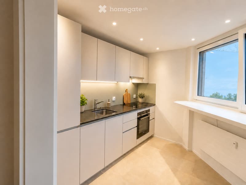 Modern kitchen with white cabinets, a black countertop, a sink, an oven, and a window offering a view.