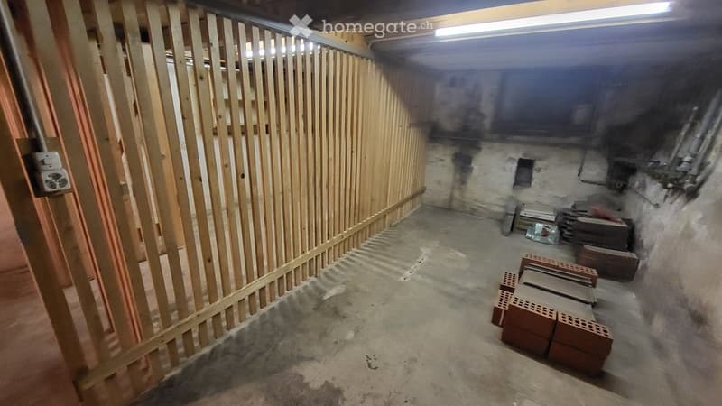 Empty basement space with unfinished concrete floor, exposed wooden framing, and scattered construction materials including bricks and wooden planks.