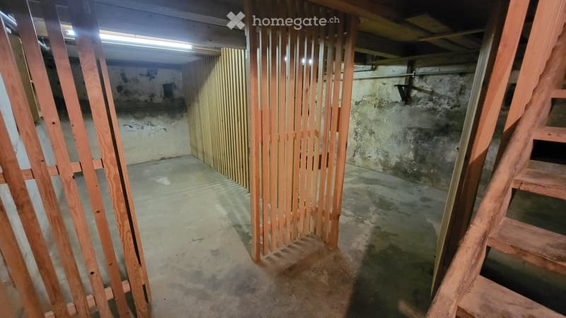 Empty basement space with unfinished concrete walls and floor, wooden framing, and a staircase leading upwards.