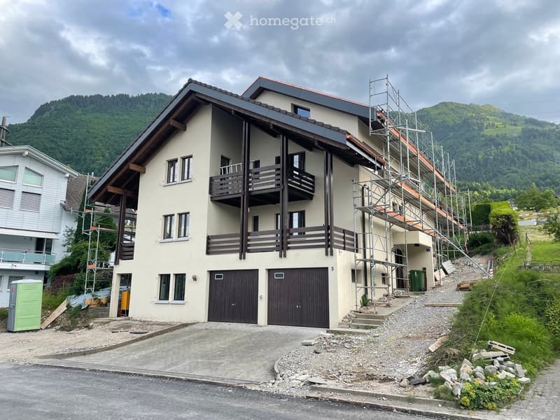 Two-story house with beige walls, dark brown garage doors, and balconies on the upper level, surrounded by a scenic mountainous landscape.