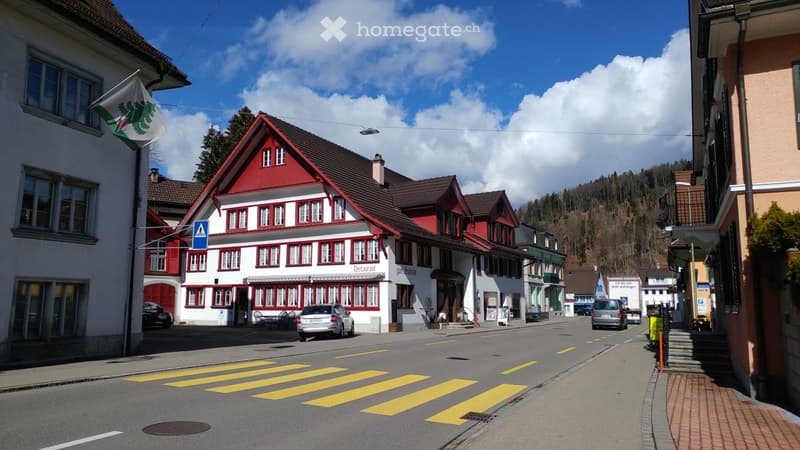 Building. A picturesque street lined with traditional Swiss houses, featuring red and white facades, multiple windows, and a clear blue sky overhead.
