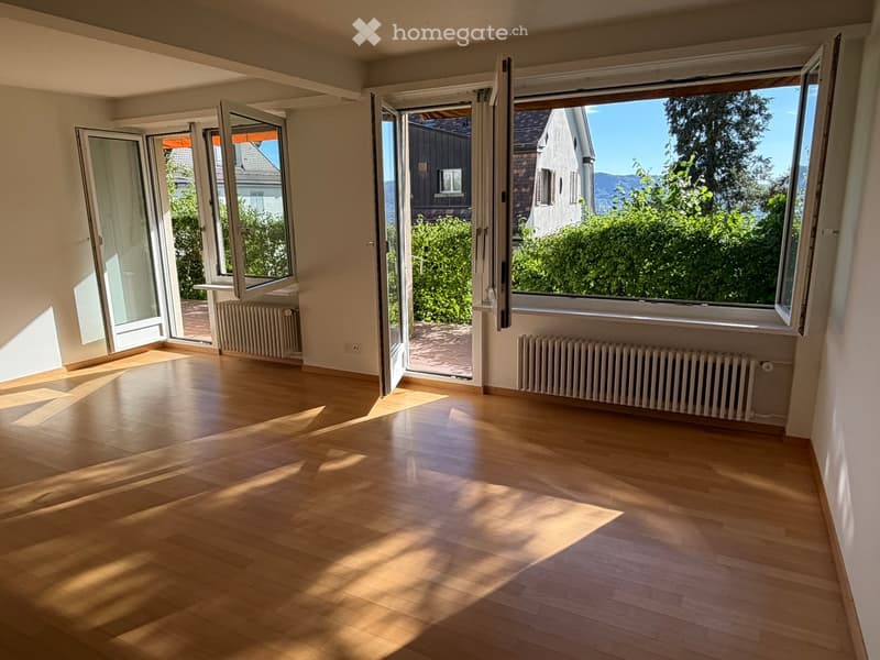 Empty room with wooden flooring, large windows, and radiators, featuring bright natural light and open views of the outdoors.