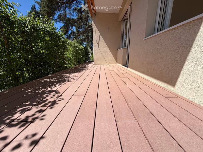 Wooden deck attached to a building, with a view of greenery and trees in the background.