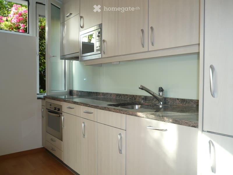 Modern kitchen with light wood cabinets, granite countertop, stainless steel microwave, oven, and sink with faucet.