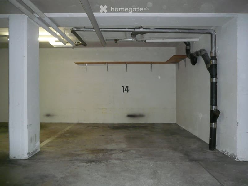 Empty underground parking space with concrete floor, white walls, and numbered stall14. Exposed pipes and lighting fixtures are visible.