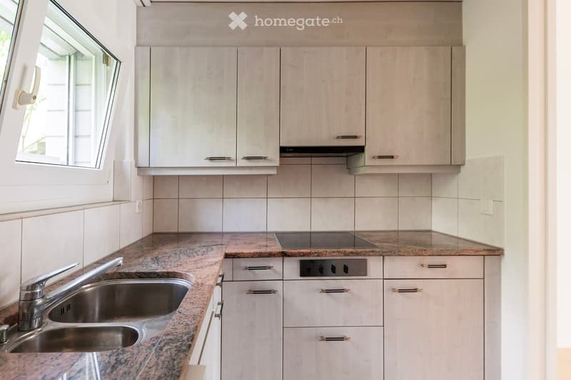 Modern kitchen with light-colored cabinets, granite countertop, stainless steel sink, and built-in stove.