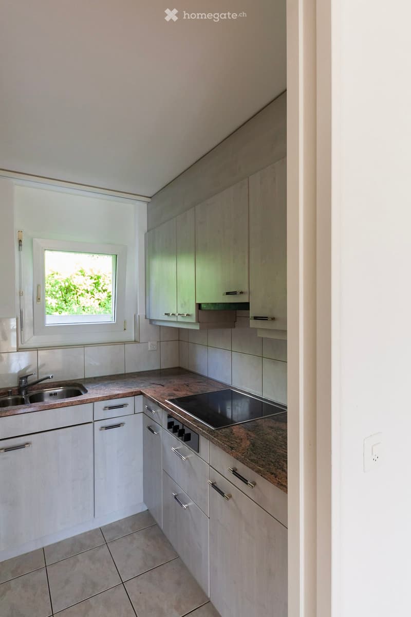 Modern kitchen with white cabinets, granite countertop, stainless steel sink, and built-in stove. Features a large window with a view of greenery.