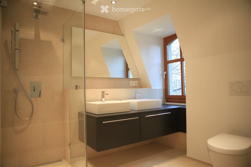 modern bathroom with two sinks, shower, toilet, mirror, and window