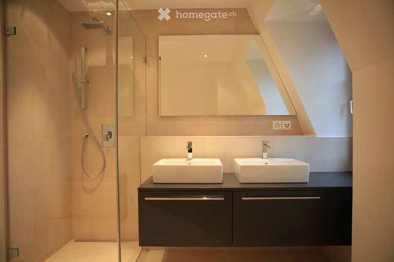 modern bathroom with two sinks, mirror, shower, and tiled walls
