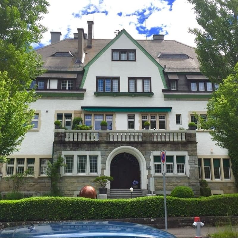 2 story house, white exterior, brown roof, balcony, multiple windows, front door, garden, trees