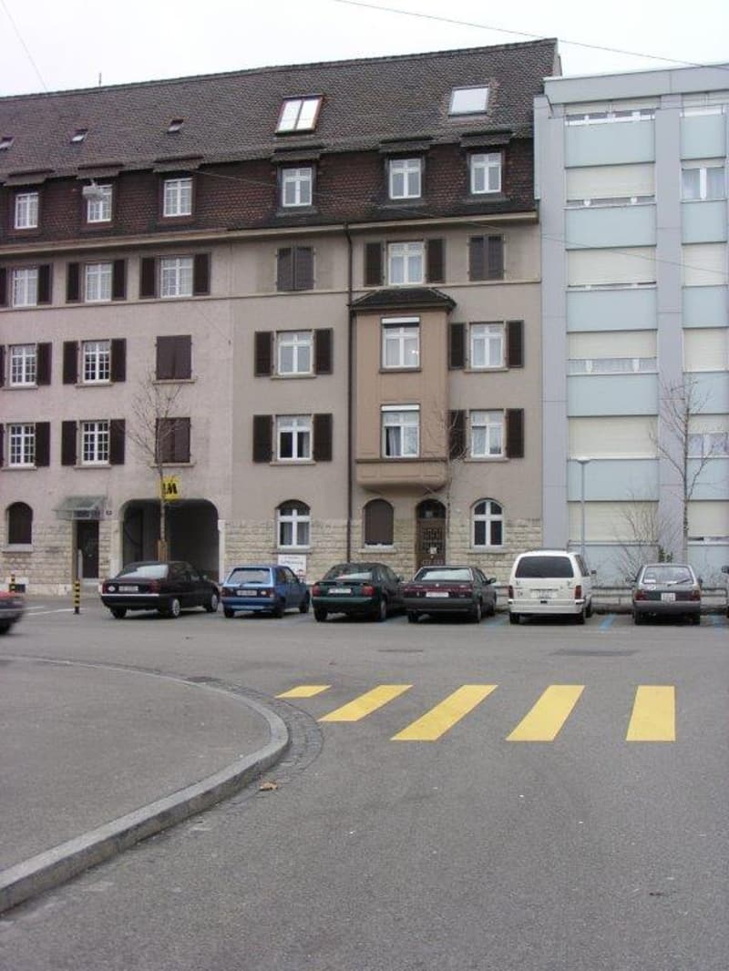 Multi-story residential building with multiple windows and a tiled roof, with several parked cars in front.