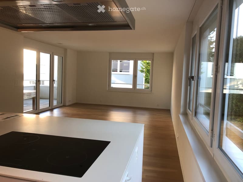 Modern kitchen with white countertops, induction stove, large windows, and sliding glass doors leading to a balcony.