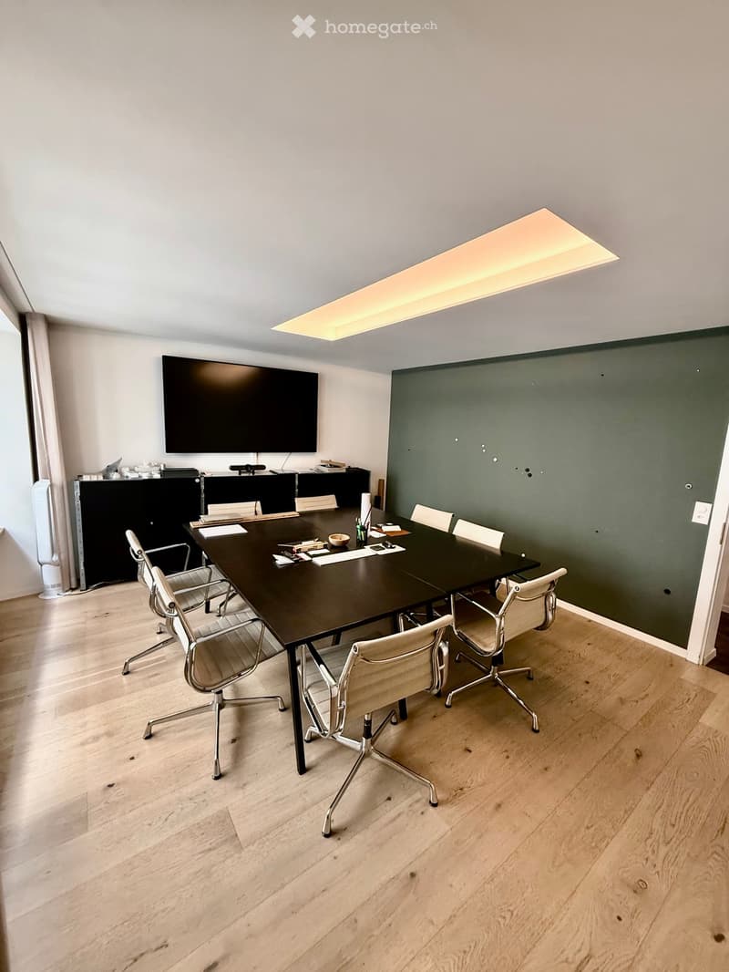 Conference room with a long black table, several chairs, a large screen, and a cabinet with office supplies.