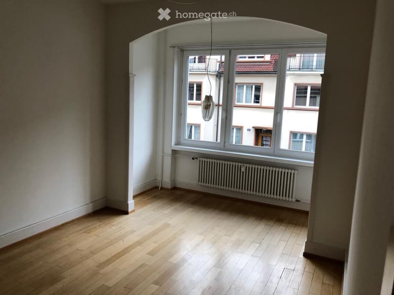 empty room, wooden floor, white walls, arch window with view of a building, radiator
