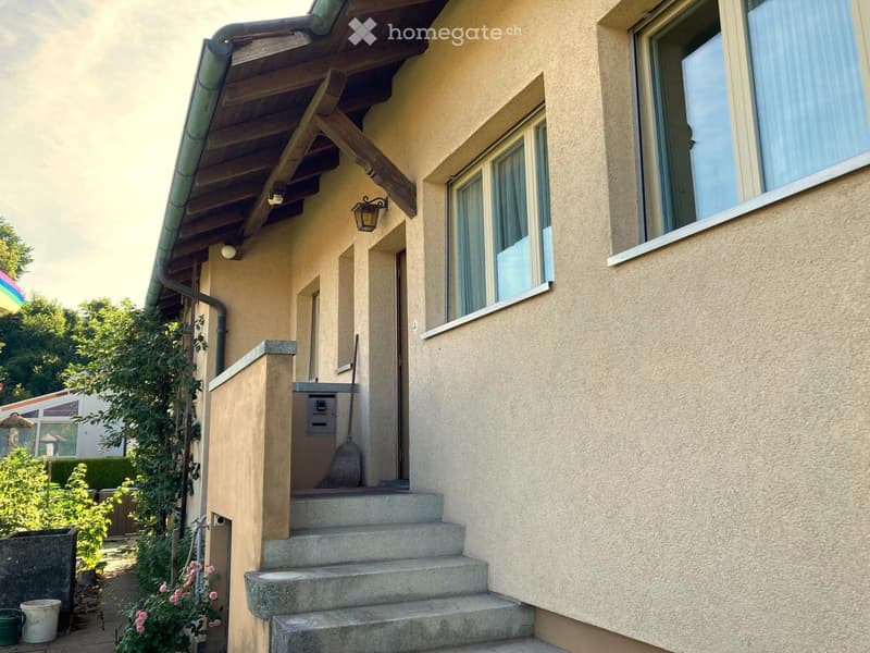 A beige house with a wooden roof, concrete steps, and a small garden.