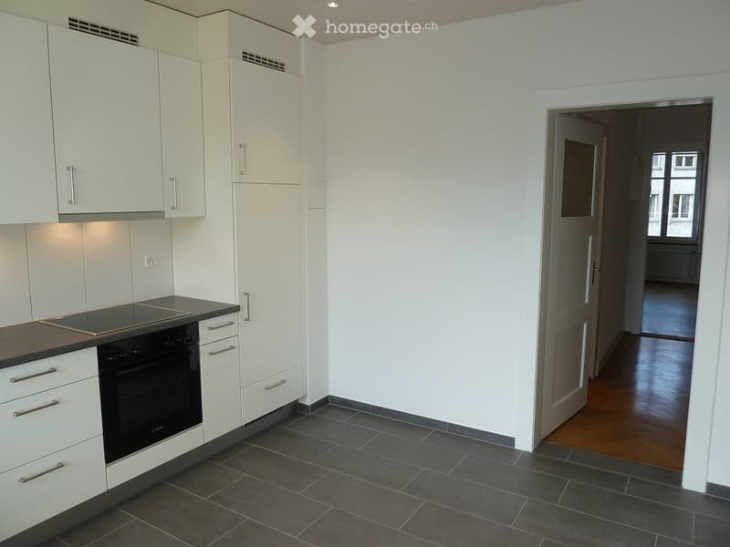 Modern kitchen with white cabinets, dark countertops, and a built-in oven. The floor is tiled in dark gray, and the walls are white.
