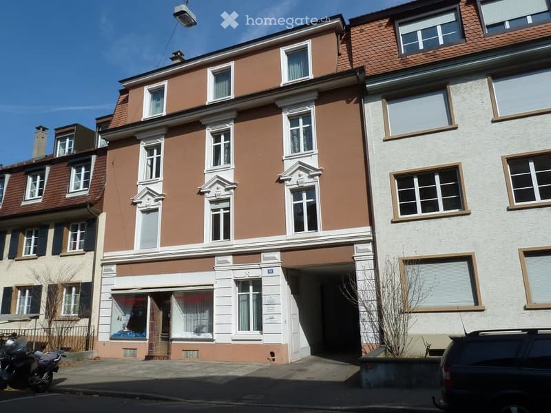 Multi-story residential building with brown and white facade, multiple windows, and a storefront at the ground level.