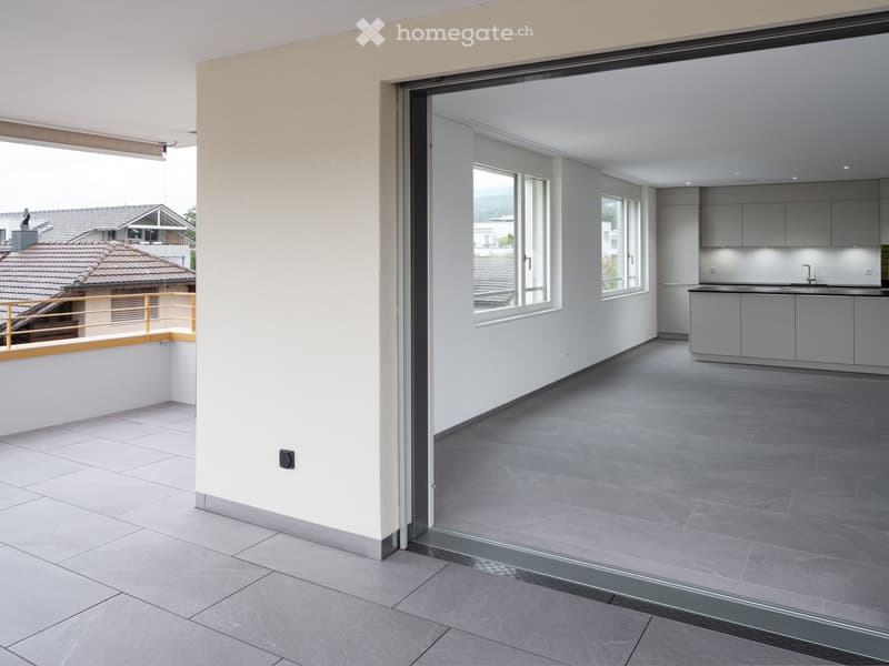 Modern, open-plan space with a balcony, grey tiled floor, grey kitchen cabinets, and a sink.