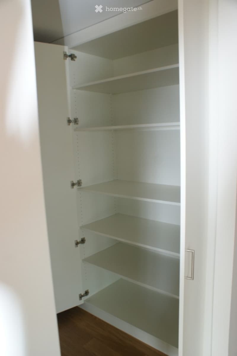 Empty white pantry with multiple shelves and a wooden floor.