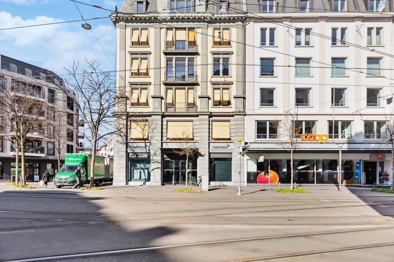 Multi-story building with balconies, storefronts, and signage for 'Coop' and 'Credit Suisse'.