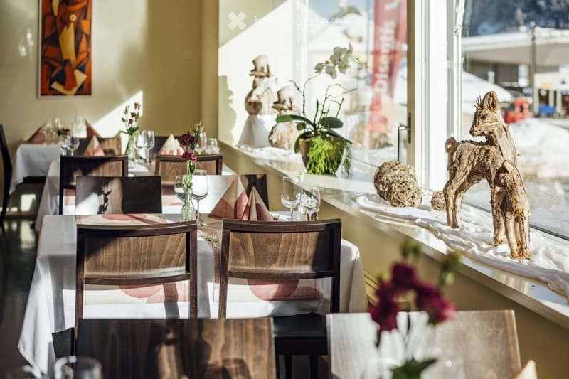 Elegant restaurant interior with wooden tables, chairs, wine glasses, napkins, floral arrangements, and decorative sculptures.