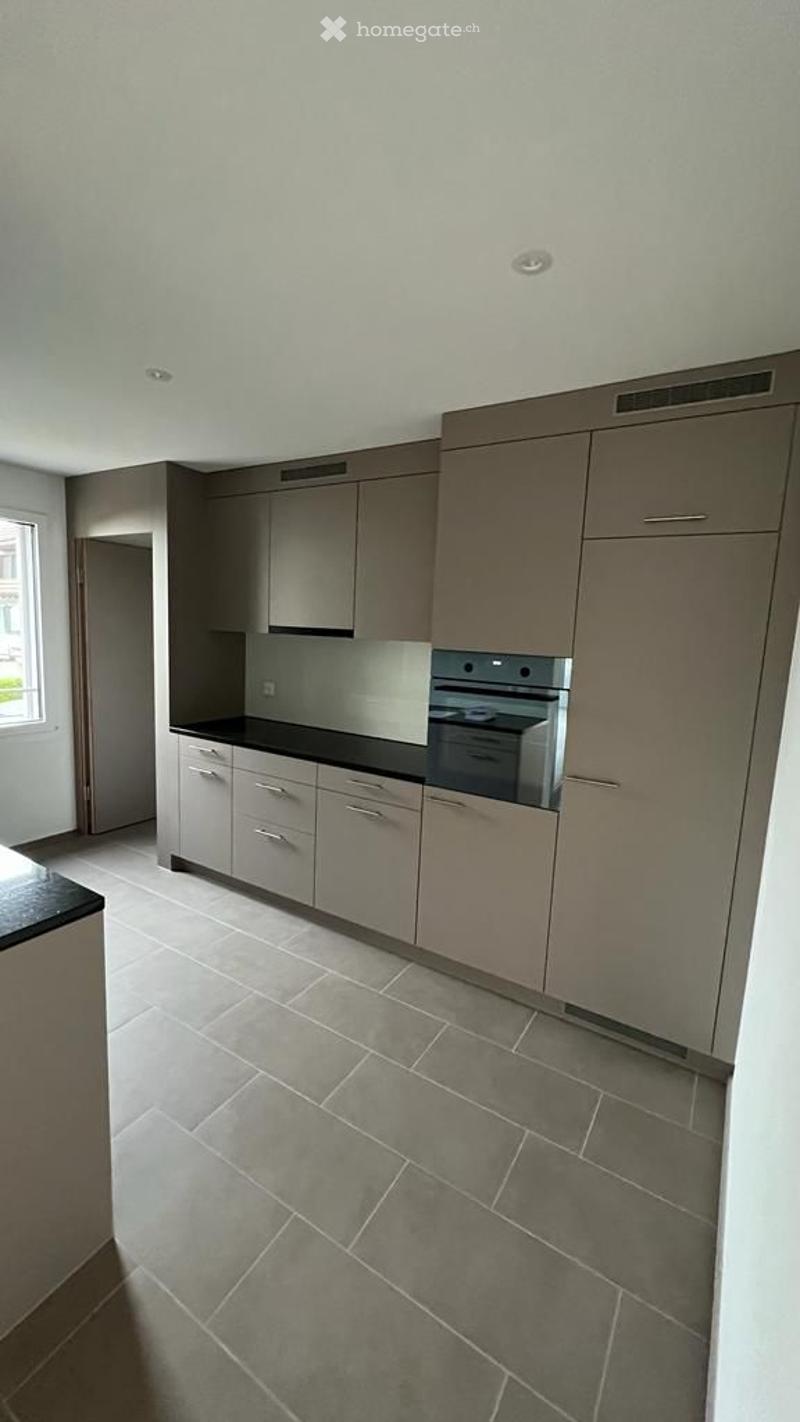 Modern kitchen with grey cabinets, black countertop, and built-in oven. Grey tiled floor and white walls.