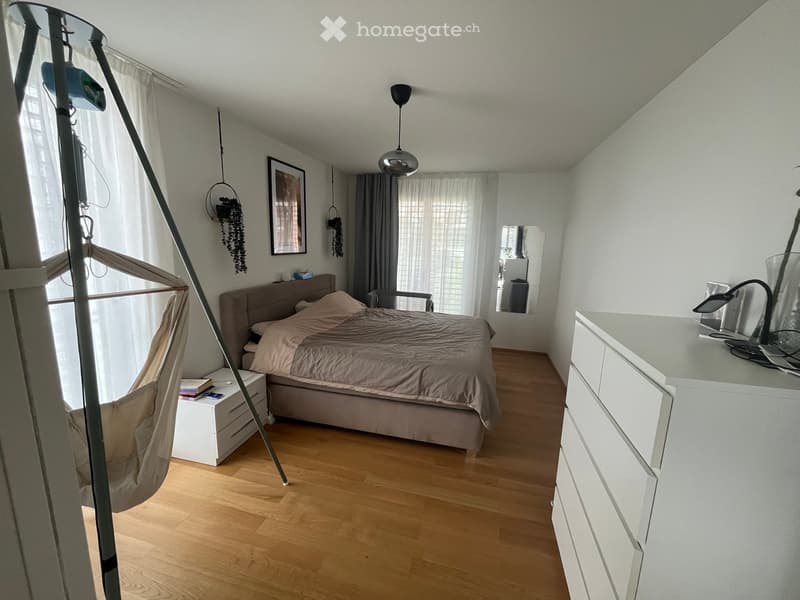 Modern bedroom with a large bed, nightstand, mirror, hanging chair, and decorative elements.
