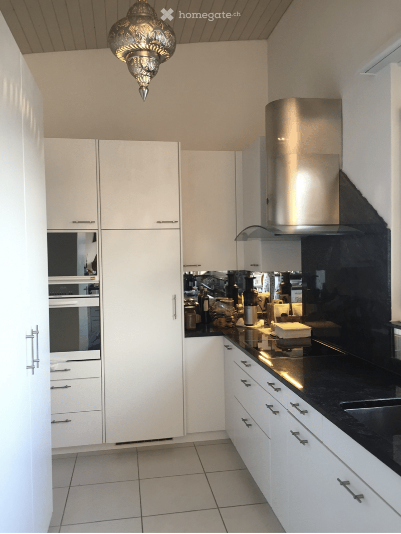 Modern kitchen with white cabinets, stainless steel appliances, black countertop, and a decorative hanging light fixture.