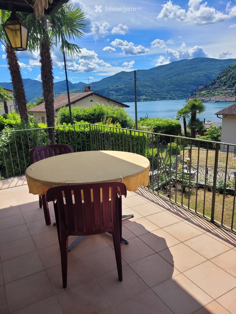 Balcony with a round table and chairs, overlooking a scenic lake and mountains.