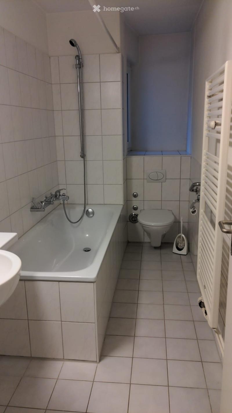 A small bathroom with a bathtub, toilet, and showerhead, featuring tiled walls and floor.