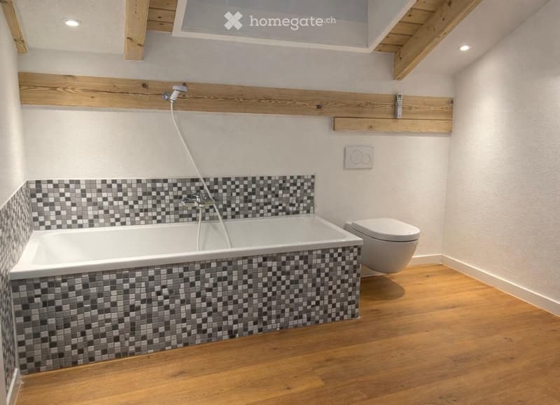 Bathroom with wooden floor, white bathtub, white toilet, tiled wall, wooden beams on ceiling