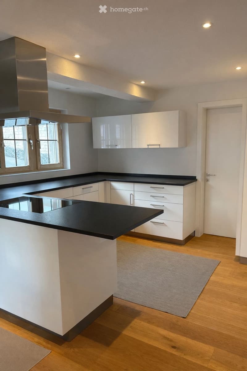 modern kitchen with island, white cabinets, black countertops, stainless steel range hood, wooden floors, large window