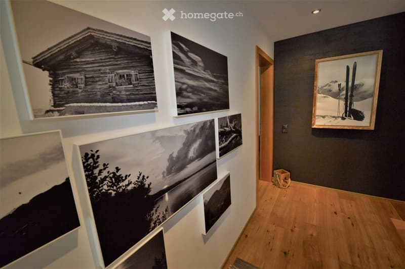 A hallway with wooden flooring and several large framed photographs displayed on the walls, including images of a cabin, landscapes, and a pair of skis.