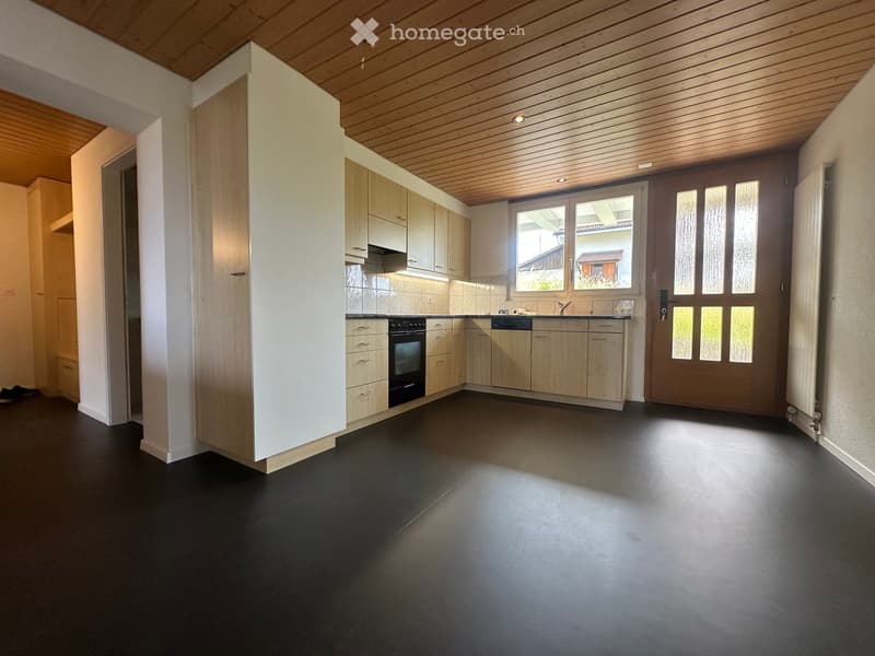 Modern kitchen with light wooden cabinets, black oven, sink, and dark flooring.