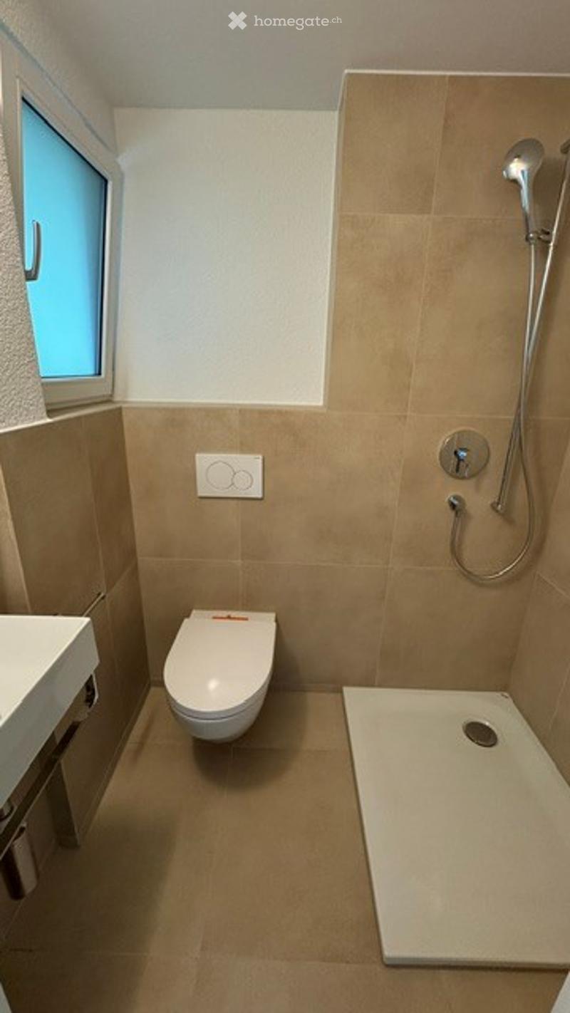 Modern bathroom with beige tiles, a toilet, a shower, and a sink.