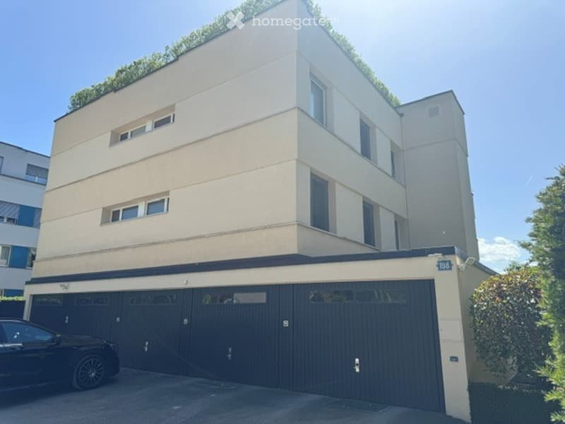 Modern multi-story building with a flat roof, large garage doors, and multiple windows.