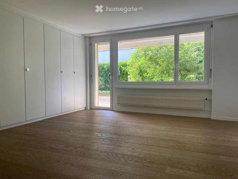 Empty room with wooden flooring, white walls, large window, and built-in closet. No furniture or equipment present.