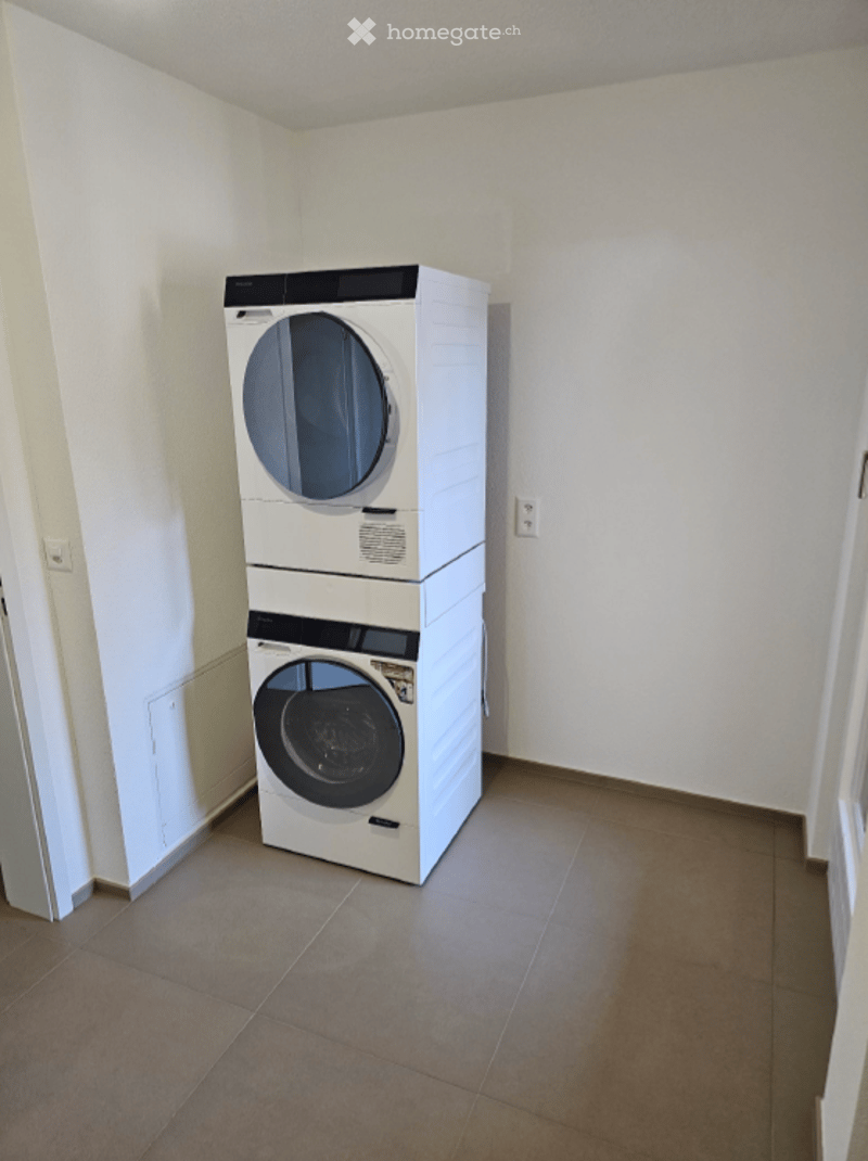 Empty room with tiled floor and white walls, featuring a stacked washer and dryer unit against one wall.
