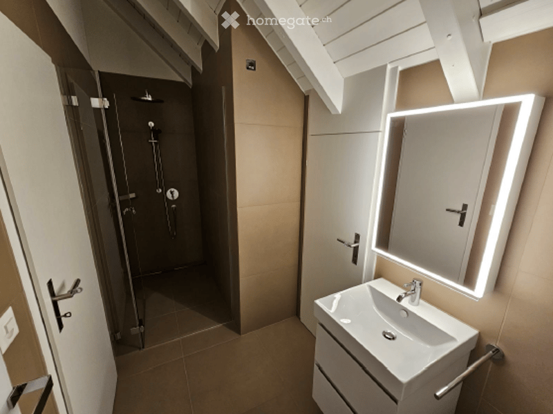 Modern bathroom with a white sink, illuminated mirror, and a separate shower stall. The space features clean lines and neutral tones.