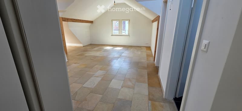 Empty attic space with exposed wooden beams, tiled floor, and a skylight window. No furniture or equipment present.