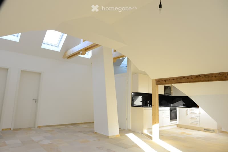 empty room, tiled floor, white walls, multiple attic windows, kitchen area, light fixtures