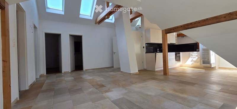 Bright, open-plan living and dining area with tiled flooring, white walls, and skylights. Adjacent modern kitchen features white cabinets, stainless steel appliances, and ample natural light.