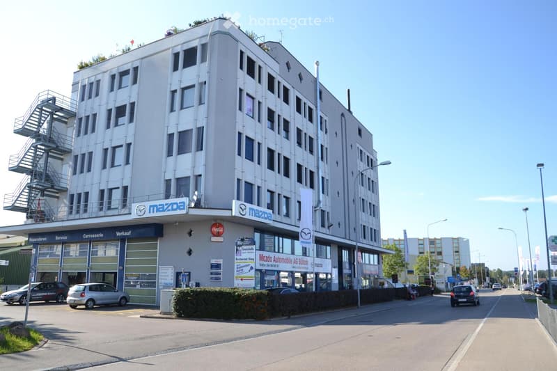 An office building with a ground floor car shop and parking lot in front.